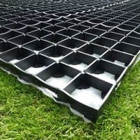 Black plastic grid-style shed base kit on grass, featuring interlocking square cells for stability and drainage.