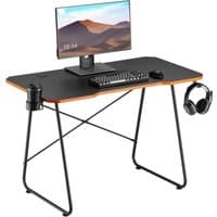 Black and orange gaming desk with monitor, keyboard, mouse, cup holder, and headphone hook.