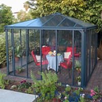 Grey 12x12 Palram Canopia Ledro 3600 gazebo with glass walls, pitched roof, and red patio furniture inside.