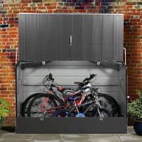 Anthracite metal garden bike storage unit with lift-up lid, housing two bicycles, against a brick wall.
