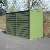 Green metal lean-to shed with sloped roof, vertical door, and horizontal paneling, set against a brick wall.