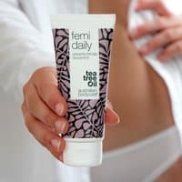 White tube of Australian Bodycare Femi Daily with purple leaf pattern and tea tree oil label, held in hand.