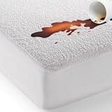 Bed'Ore waterproof mattress protector with terry top, deep fitted skirt, absorbing spilled liquid from a cup.