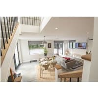 Modern living room with beige sofa, wooden dining table, large windows, and staircase with black railings.