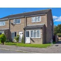Brick semi-detached house with white door, bay window, and pitched roof, surrounded by green lawn and shrubs.