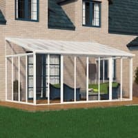 White Palram Canopia SanRemo lean-to conservatory with clear panels, attached to brick house, featuring patio furniture.