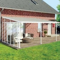 White 13' Palram Canopia patio cover side wall with clear panels attached to a brick house over a wooden deck.