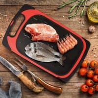 Black and red Avilo 2 in 1 defrost tray and cutting board with raw meat, fish, and shrimp on a wooden surface.