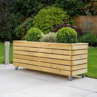 Wooden garden planter with slatted design, rectangular shape, and wheels, filled with green shrubs.
