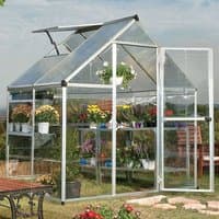 Silver polycarbonate greenhouse with clear panels, angled roof, and open door, showcasing plants on shelves inside.