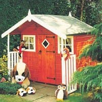 Red wooden playhouse with white trim, diamond window, porch, and stuffed animals on railing, surrounded by greenery.