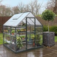 Grey polycarbonate greenhouse with clear panels, pitched roof, and metal frame, housing various plants on shelves.