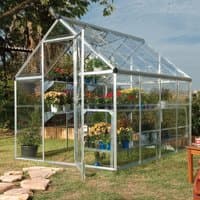 Silver polycarbonate greenhouse with clear panels, pitched roof, and walk-in door, housing potted plants inside.