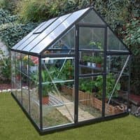 Grey polycarbonate greenhouse with clear panels, pitched roof, and door, surrounded by plants and grass.