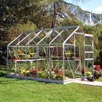 Green aluminum-framed greenhouse with clear panels, pitched roof, and sliding door, filled with colorful plants.