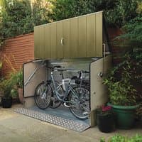 Green metal bike shed with ramp, featuring a sloped roof and open front, housing two bicycles inside.