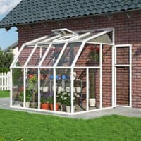 White lean-to greenhouse with clear panels, attached to brick wall, featuring sloped roof and door, housing potted plants.