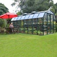 8x16 Palram Canopia Rion Clear Grand Gardener Greenhouse with dark frame, clear panels, and roof vents in a garden setting.