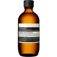 Amber bottle of Aesop Parsley Seed Facial Cleansing Oil, black cap, white label with black text, 200 ml.