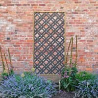 Grey wooden diamond lattice panel with a natural frame, set against a brick wall with surrounding greenery.