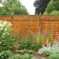 Wooden diamond lattice trellis fence topper, 6' x 1', natural finish, atop a solid fence panel in a garden setting.