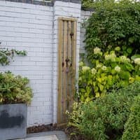 Vertical slatted garden screen panel, pressure treated wood, 6' x 1', against white brick wall with greenery.