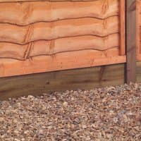 Wooden gravel board, 6' x 6", pressure treated, light brown with natural grain, set against gravel and fencing.