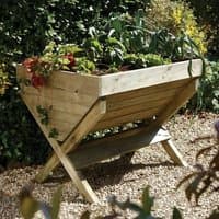 Wooden Forest Garden trough planter with angled legs, filled with green plants, on a gravel surface.