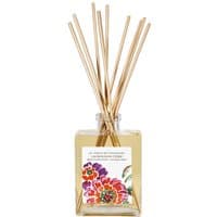Square glass bottle with floral label, filled with yellow liquid, topped with natural reed sticks.