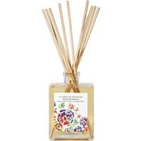 Square glass bottle with floral label, filled with yellow liquid, topped with natural reed sticks.