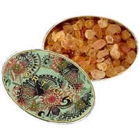 Oval tin with colorful ornate design, containing amber-colored scented crystals by Ortigia.