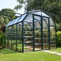 Green Palram Canopia Rion Grand Gardener 8x8 greenhouse with clear panels and a peaked roof, set in a garden.