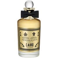 Clear glass bottle with golden liquid, black bow tie, round cap, and ornate label reading "Penhaligon's Cairo Eau de Parfum."