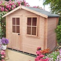 Wooden log cabin summerhouse with two front windows, single door, pitched roof, surrounded by colorful flowers.