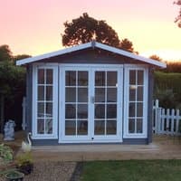 Gray wooden log cabin summerhouse with white-framed glass double doors and windows, set against a sunset backdrop.