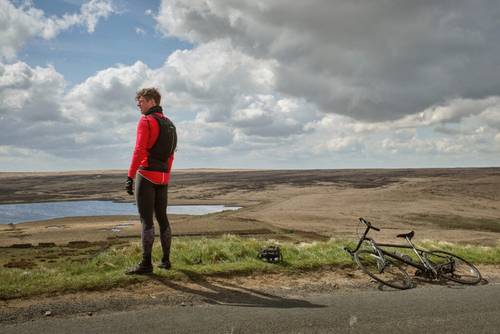 James Norton as Tommy Lee Royce in Happy Valley 3, cycling outfit above Warley Moor reservoir with bike